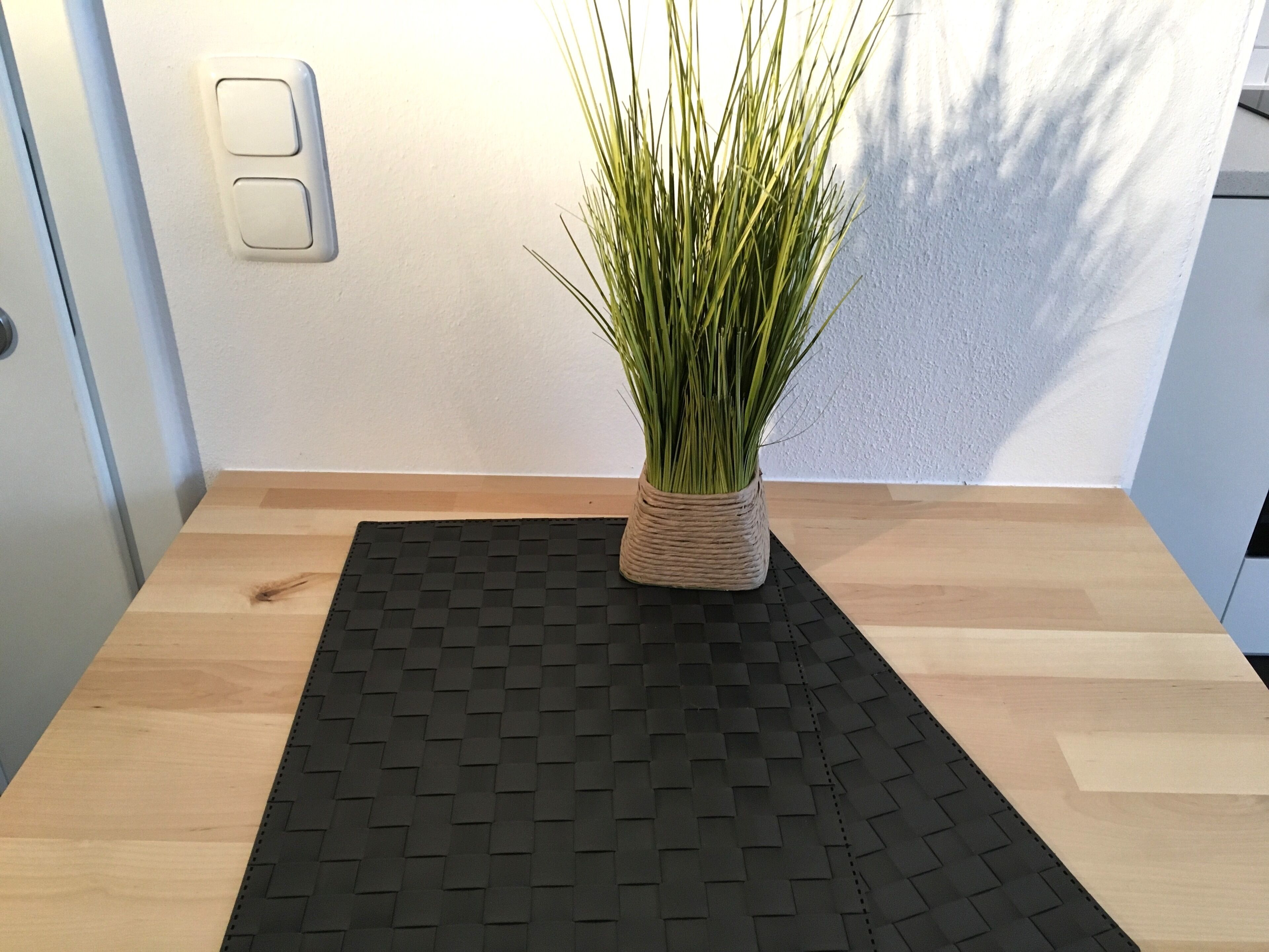 Una pequeña mesa de madera con un camino de mesa tejido negro y una planta en maceta.
