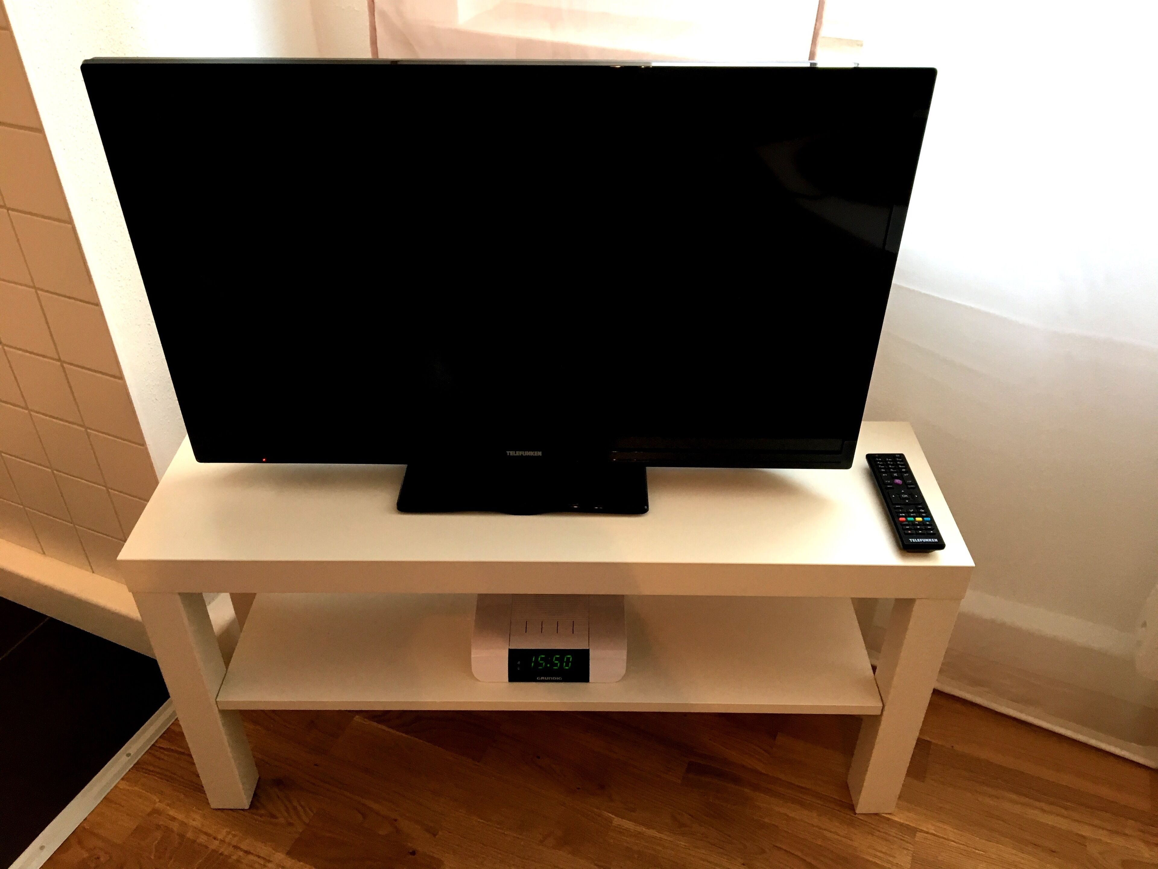 Televisor de pantalla plana sobre un mueble blanco con control remoto.