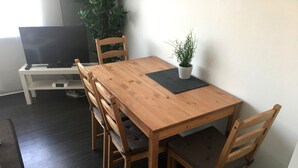 Puisesta ruokapöydästä ja kuudesta tuolista koostuva ruokailuryhmä, ruukkuistutettu kasvi ja televisio, joka on sijoitettu jalustalle.