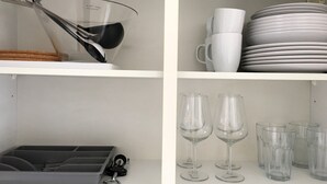 A white shelf with a wine glass rack, a stack of white plates, and a set of clear wine glasses. - Downtown (Regensburg)