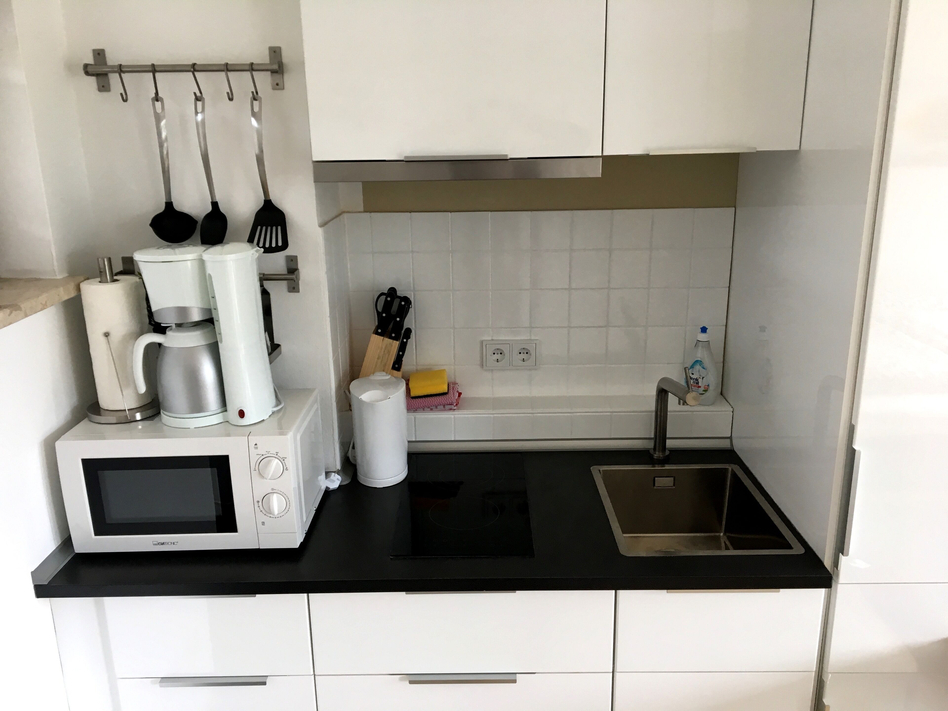 Eine moderne Küche mit weißen Schränken, einer schwarzen Arbeitsplatte, einer eingebauten Mikrowelle, einer Kaffeemaschine und einem Spülbecken.