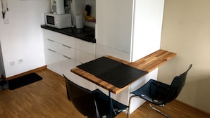 A compact kitchen with a microwave, kettle, and utensils hanging on the wall. There is a small window and a door with a handle. - Downtown (Regensburg)