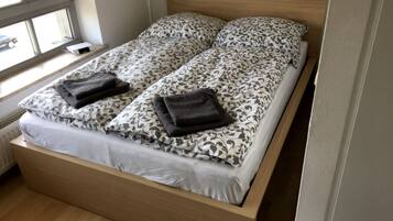 Una cama doble con ropa de cama estampada y dos toallas dobladas.