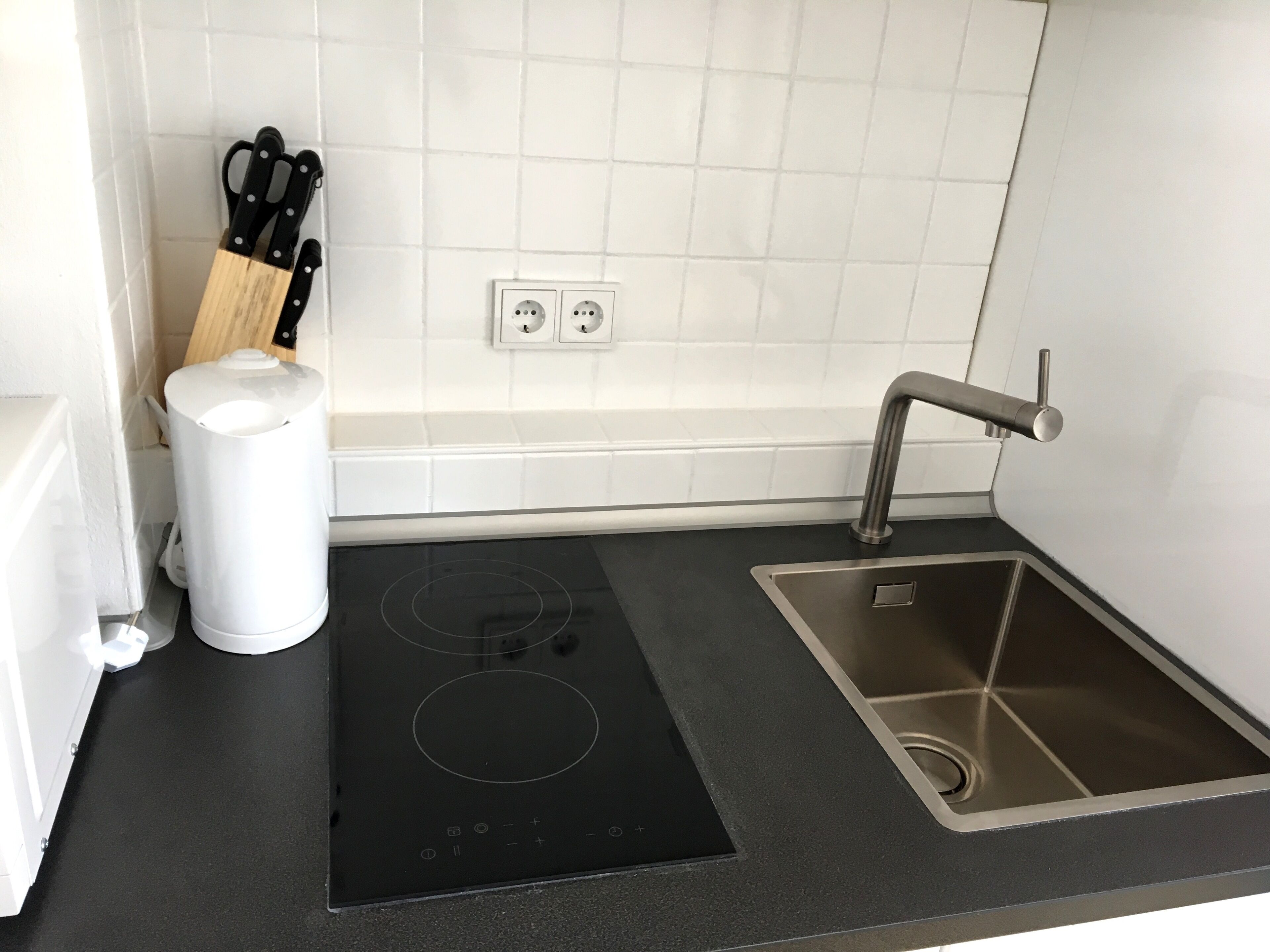 A modern kitchen with a black induction cooktop, a stainless steel sink, and a white trash bin.