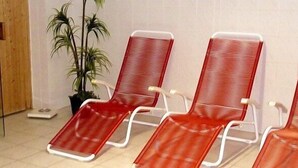 Three red lounge chairs with white frames, a potted plant, and a wooden door. - Hotel Märkischheide GmbH (Vetschau/Spreewald)