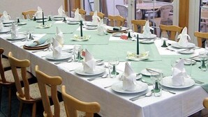 A long dining table set with white tablecloths, plates, and napkins, surrounded by wooden chairs. - Hotel Märkischheide GmbH (Vetschau/Spreewald)