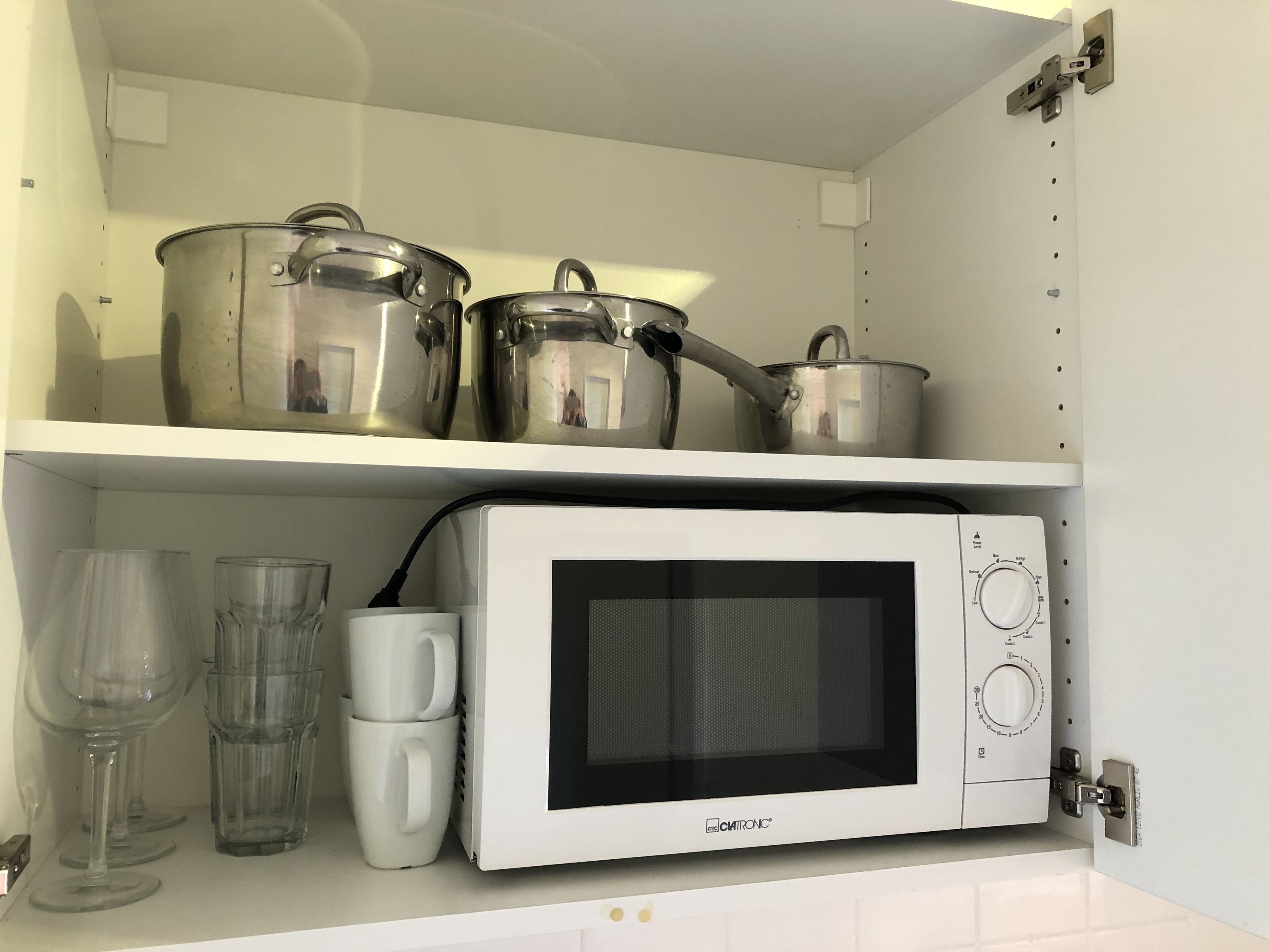 Een keuken met een magnetron, twee pannen en twee glazen op een plank.