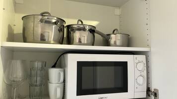 Een keuken met een magnetron, twee pannen en twee glazen op een plank.