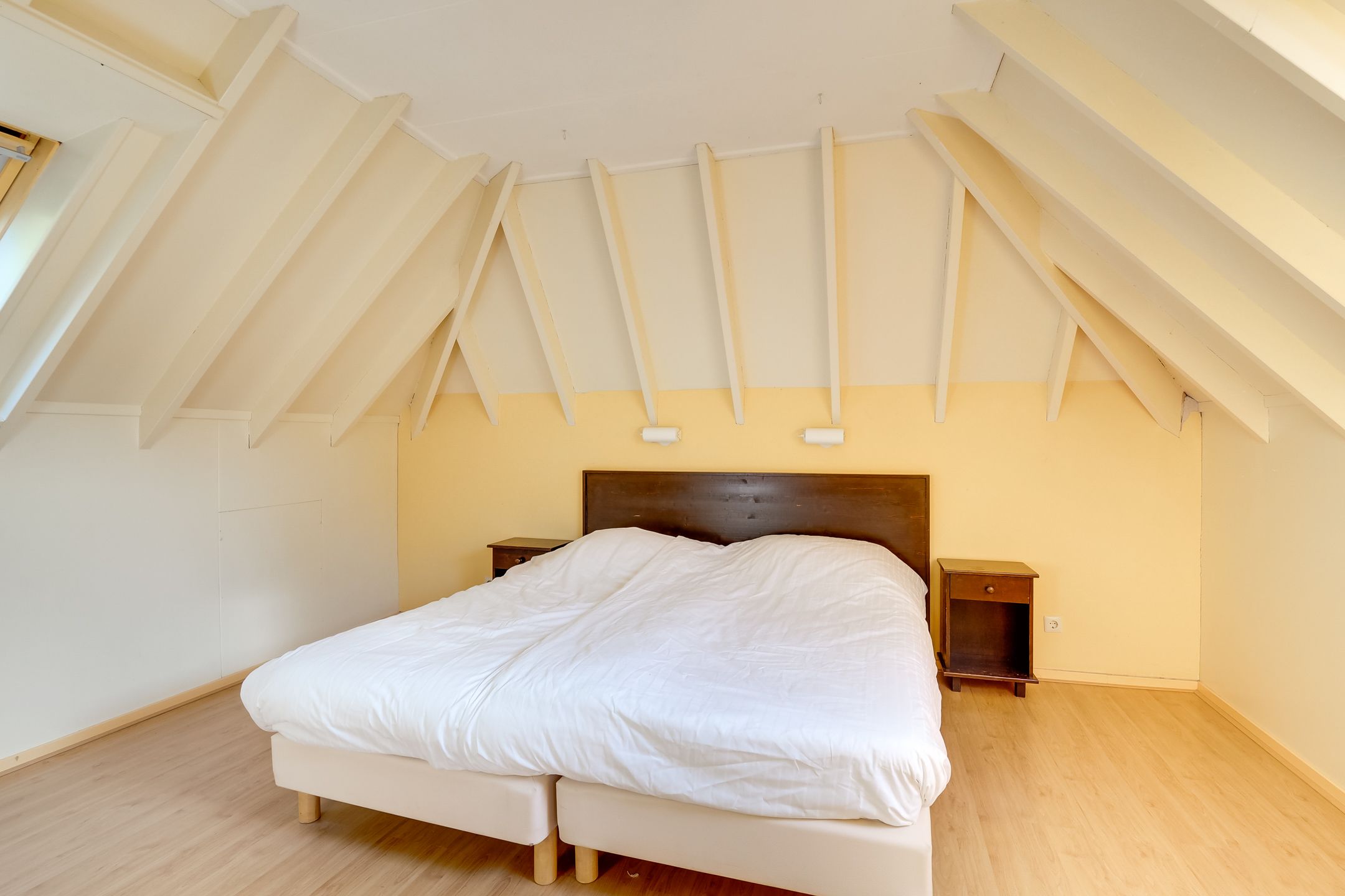 A bedroom with a sloped ceiling, a bed, two bedside tables, and a wooden floor.