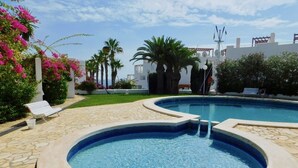 A swimming pool with a stone deck, surrounded by palm trees and flowering plants. - VILLA LOS REMOS SEAVIEW (Mojácar)