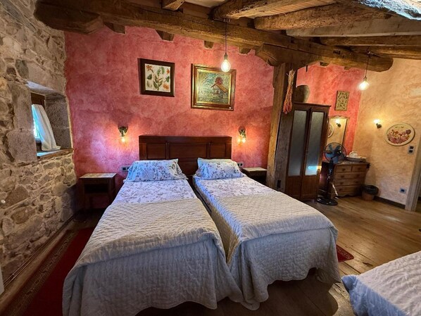 A rustic room with two beds, stone walls, wooden beams, and artwork on the walls. - Garzibaita country house near San Sebastián. (Sunbilla)