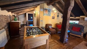 Een gezellige kamer met een tafelvoetbaltafel, houten balken, stenen muren en een comfortabele zithoek met een bank en fauteuils.