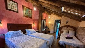 Een landelijke kamer met drie bedden, houten balken en kunstwerken in lijsten aan de wanden.