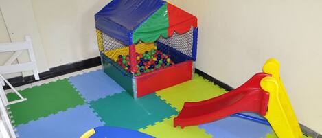 Zona de juegos con piscina de pelotas, tobogán y una mesita.