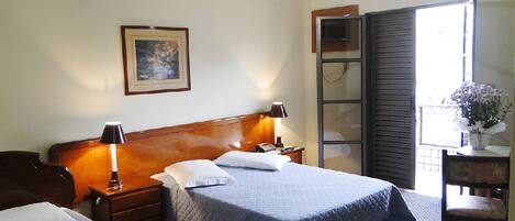 A hotel room with two beds, a wooden headboard, bedside lamps, a nightstand, a framed picture on the wall, and a window with blinds.