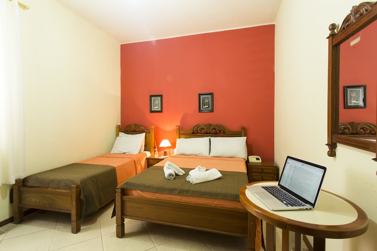 Ein Hotelzimmer mit zwei Betten, einem Laptop auf einem kleinen Tisch und einem Spiegel an der Wand.