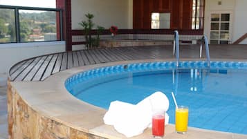 A swimming pool with a stone wall, a white towel, and two drinks on the edge.