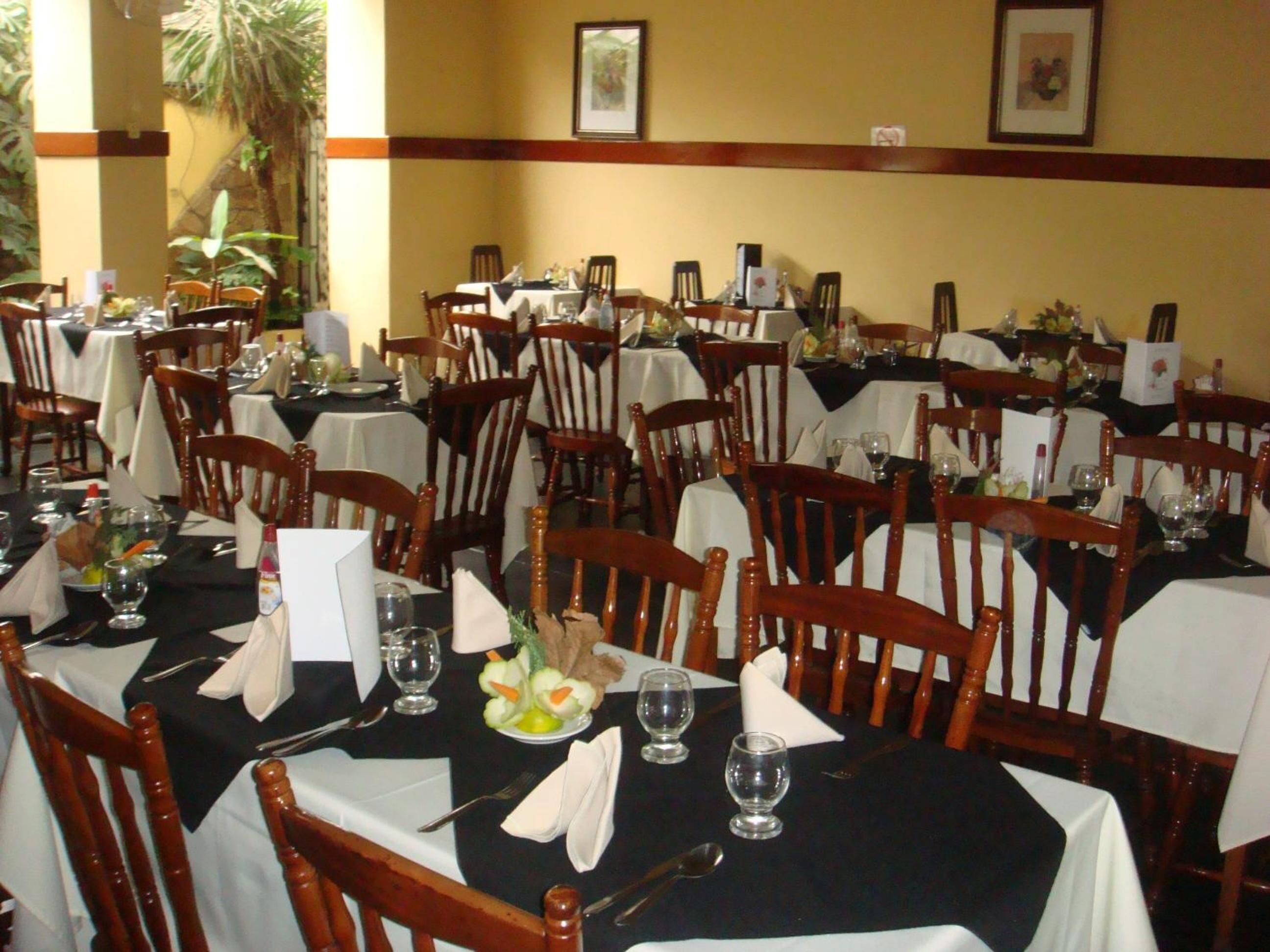 A restaurant with multiple tables, each set with chairs, white tablecloths, and various dining items.