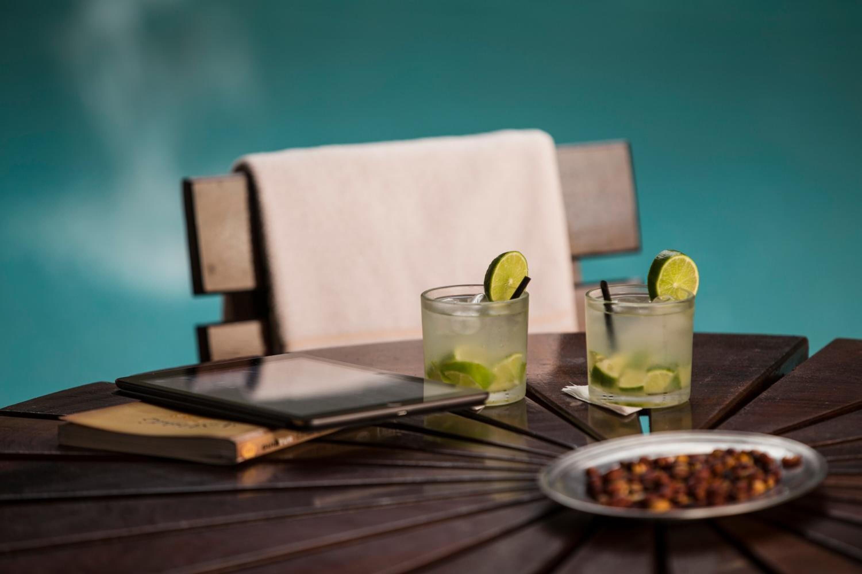 Two glasses of a lime-based drink on a wooden table with a smartphone and a bowl of nuts.