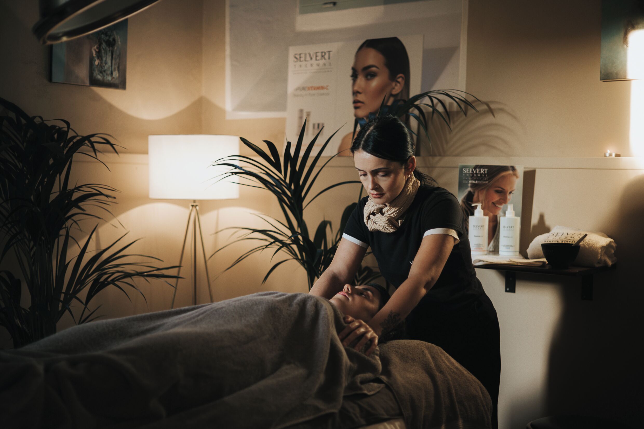 A massage therapy session in a room with a bed, a lamp, and posters on the wall.