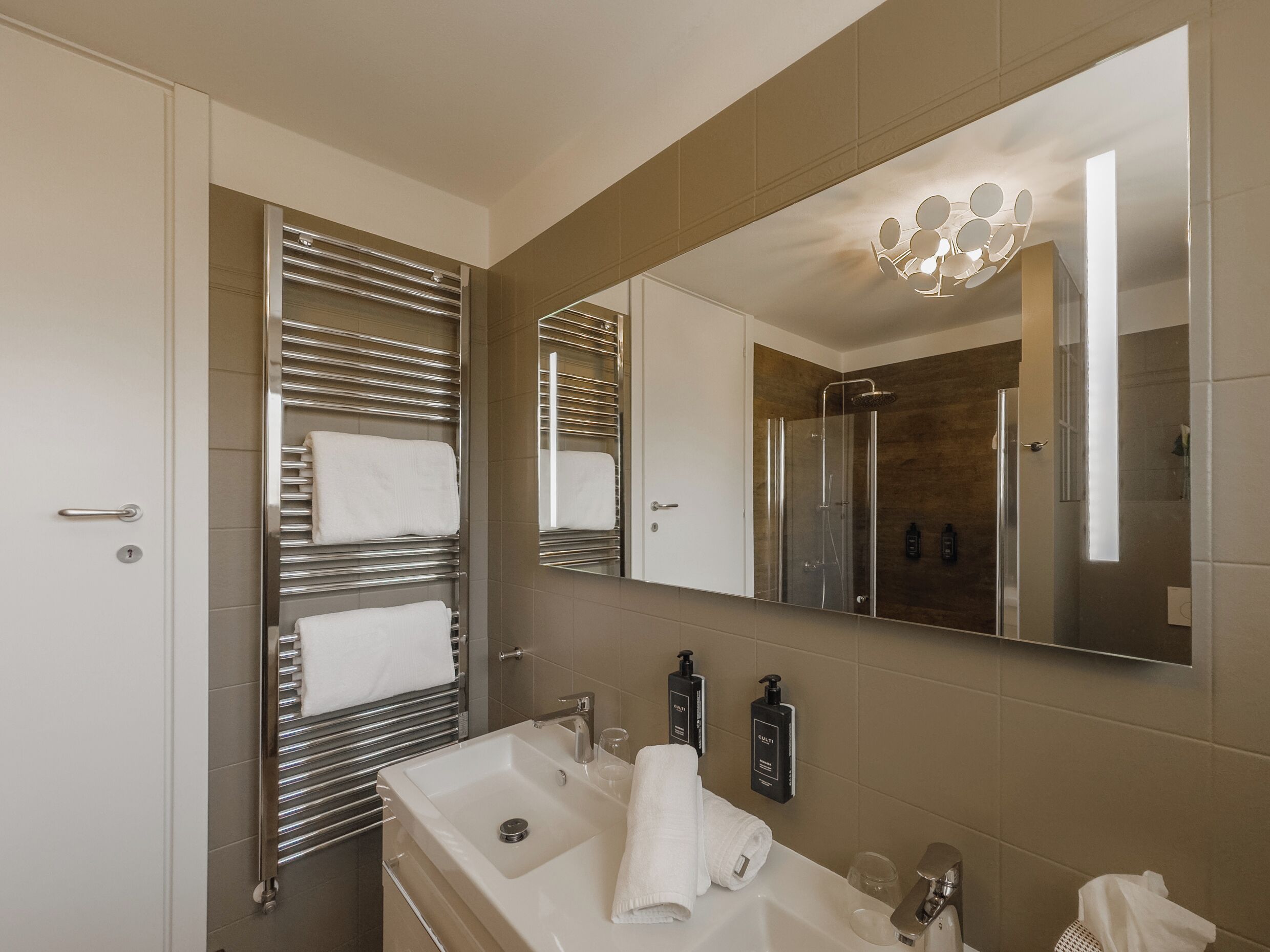 A modern bathroom with a large mirror, a sink, and a shower.