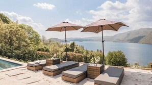 A poolside area with lounge chairs and umbrellas overlooking a lake. - Villa Antica Colonia (Pettenasco)