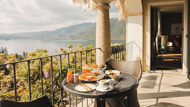 A balcony with a table set for breakfast, overlooking a lake and mountains. - Villa Antica Colonia (Pettenasco)