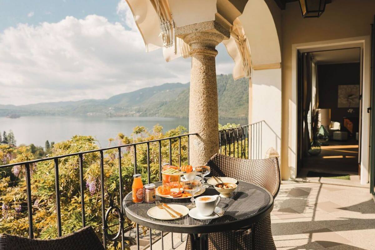 A balcony with a table set for breakfast, overlooking a lake and mountains.