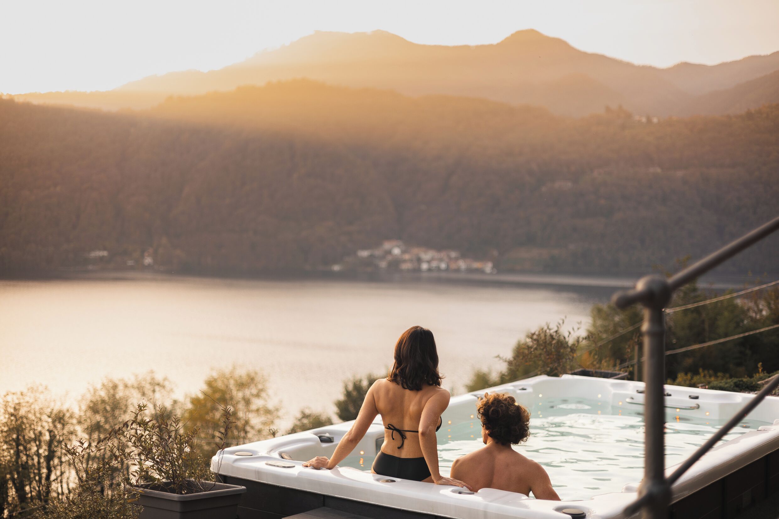 A hot tub with two people, overlooking a lake and mountains.