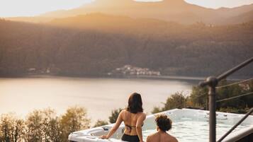 A hot tub with two people, overlooking a lake and mountains.