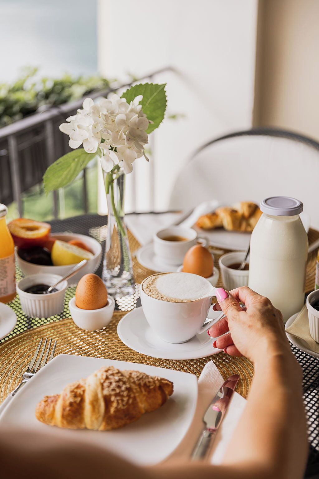 A breakfast setting with croissants, coffee, and a vase of flowers.