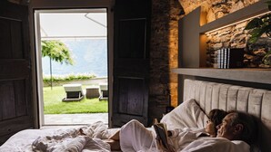 A bedroom with a bed, a stone wall, and a view of a garden. - Villa Antica Colonia (Pettenasco)