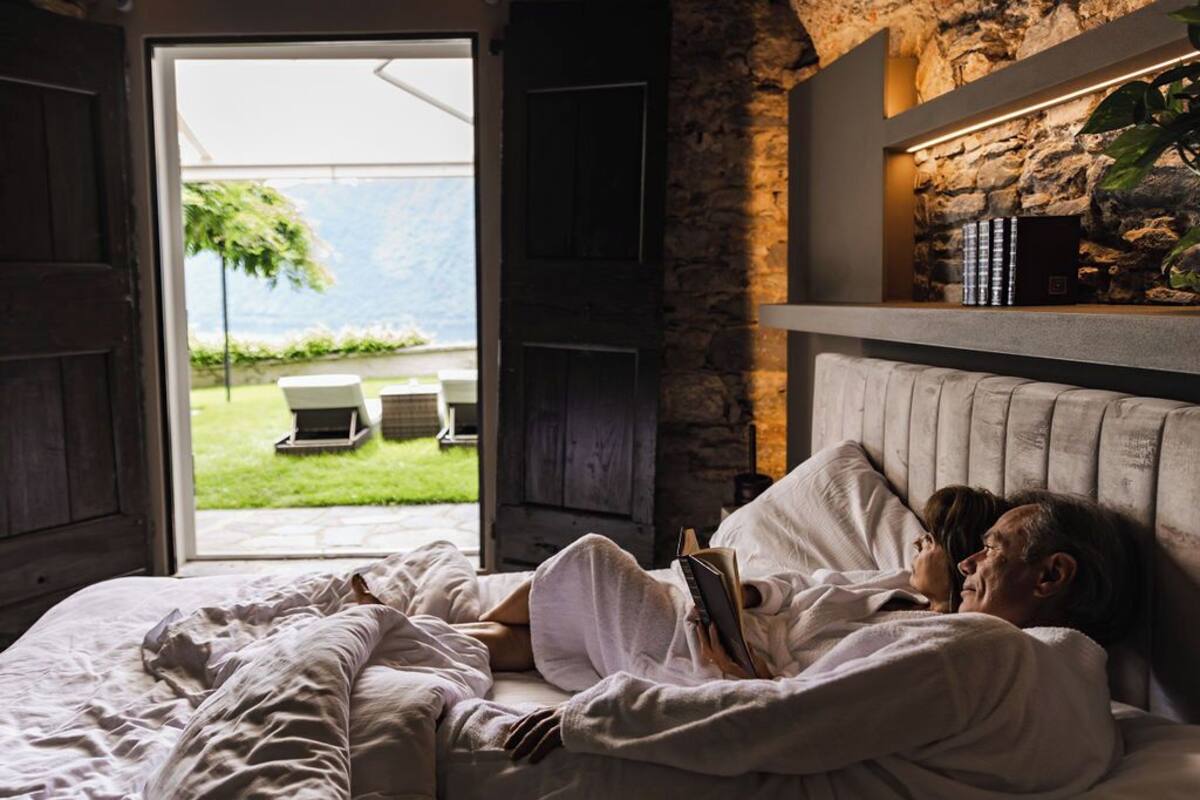 A bedroom with a bed, a stone wall, and a view of a garden.