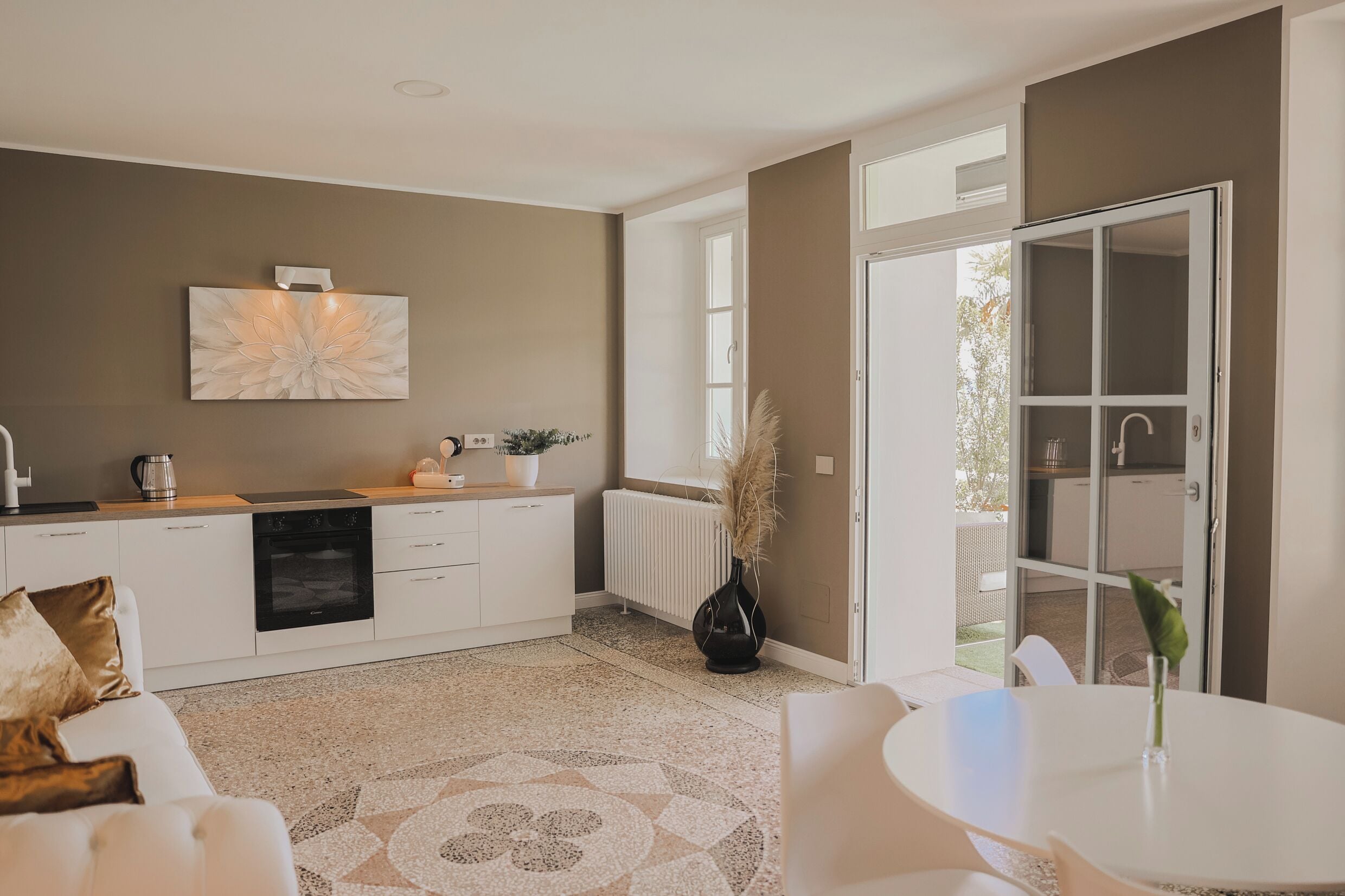 Una cocina moderna con armarios blancos, un gran cuadro de pared con flores y una zona de comedor con una mesa redonda y sillas.