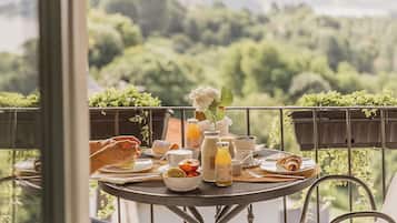 A balcony with a table set for breakfast, overlooking a lush green landscape.