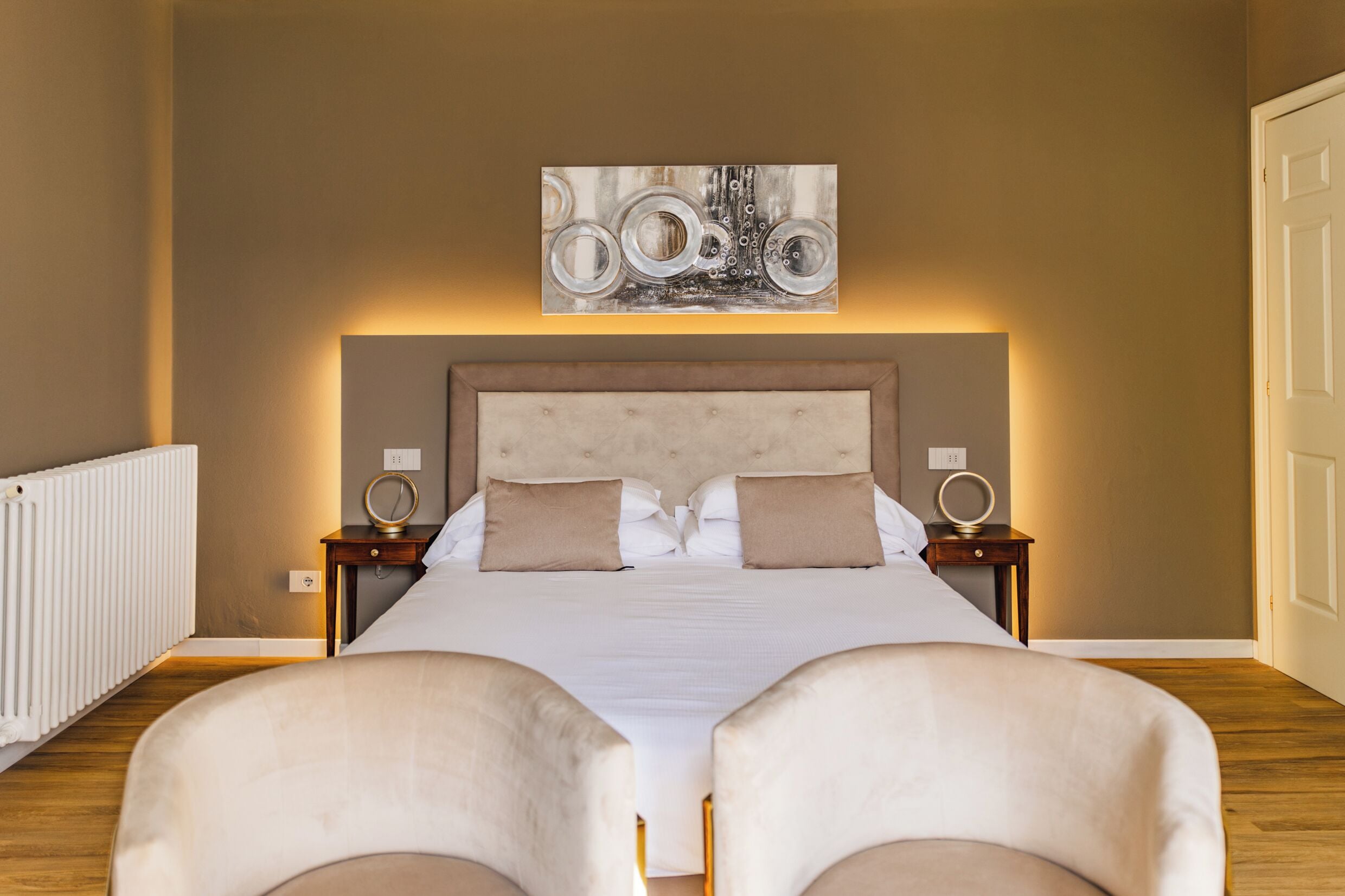 Un dormitorio ordenado con una cama grande, dos mesitas de noche y una obra de arte colgada en la pared.