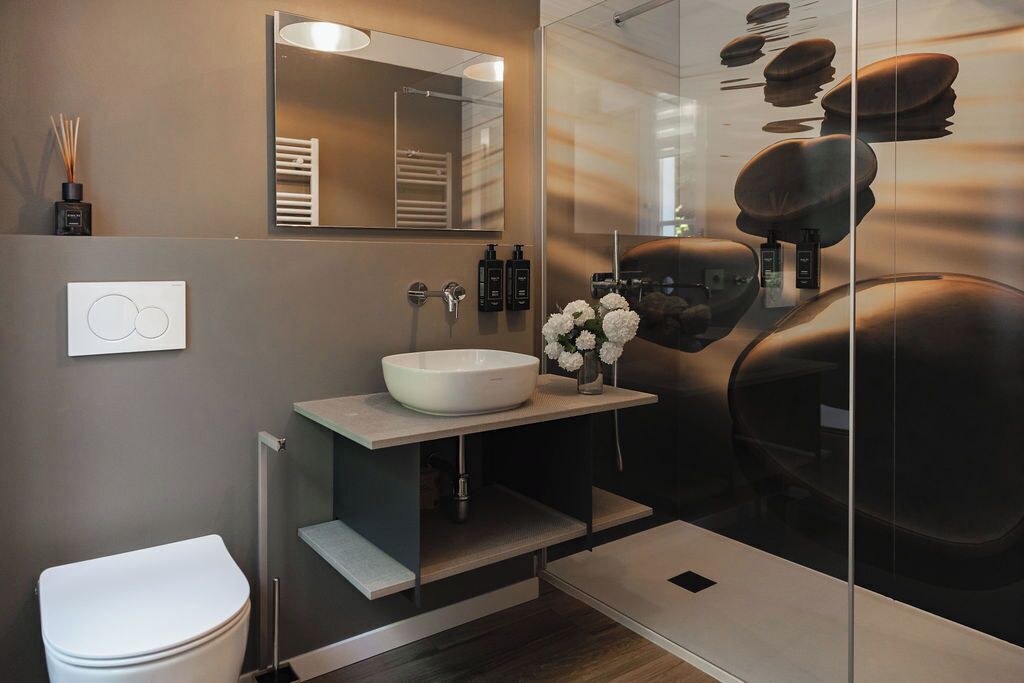 A modern bathroom with a white toilet, a large mirror, a white sink, and a glass shower enclosure.