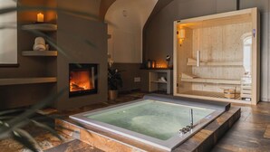 A spa room with a large hot tub, a fireplace, wooden shelves, and a sauna area. - Villa Antica Colonia (Pettenasco)