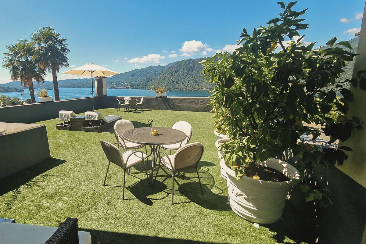 An outdoor patio with a table and chairs, a potted plant, and a view of the sea and mountains.