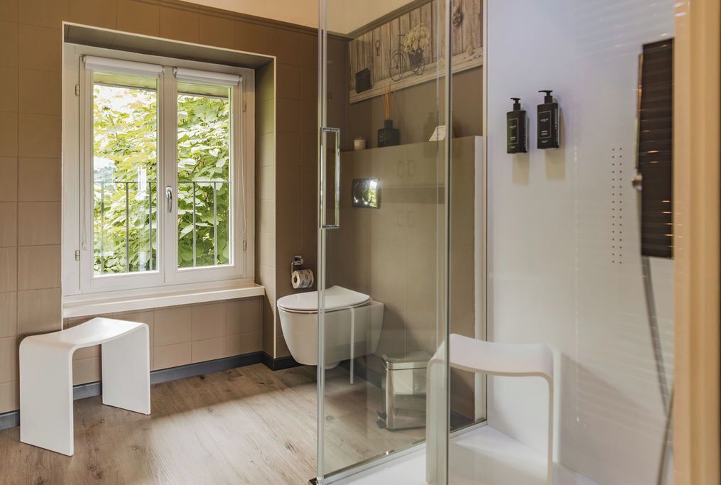 Ein modernes Badezimmer mit Duschkabine aus Glas, Toilette und einem kleinen weißen Hocker.