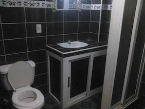 A small bathroom with a toilet, a sink, and a shower enclosure. - Casa Villa Magui (Havana)