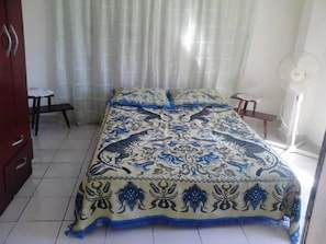 A bedroom with a bed, a nightstand, a chair, and a fan. - Casa Villa Magui (Havana)