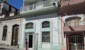 A building with a green facade, a balcony with ornate metal railings, and a sign with numbers. - Casa Villa Magui (Havana)