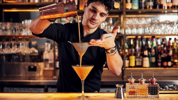 Un barman sirviendo una bebida en una copa de martini.