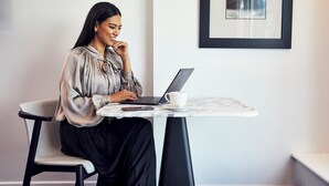 Una persona sentada a una mesa con una computadora portátil, una taza y un teléfono inteligente.