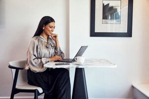 Una persona sentada a una mesa con una computadora portátil, una taza y un teléfono inteligente.