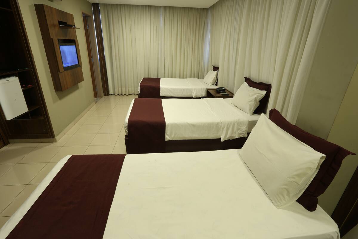 Une chambre d’hôtel avec deux lits, un téléviseur fixé au mur et une grande fenêtre avec des rideaux.