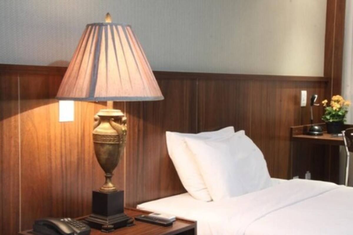 Une chambre d’hôtel avec un lit, une lampe de chevet, un téléphone et une petite table sur laquelle est posée une plante.