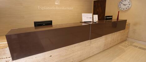 A reception desk at Esplanada Brasilia Hotel with a clock and a signboard.