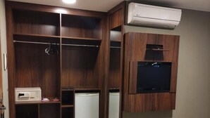 Une chambre d’hôtel dotée d’une grande armoire, d’un téléviseur à écran plat fixé au mur et d’un lit recouvert d’une couvre-lit de couleur sombre.